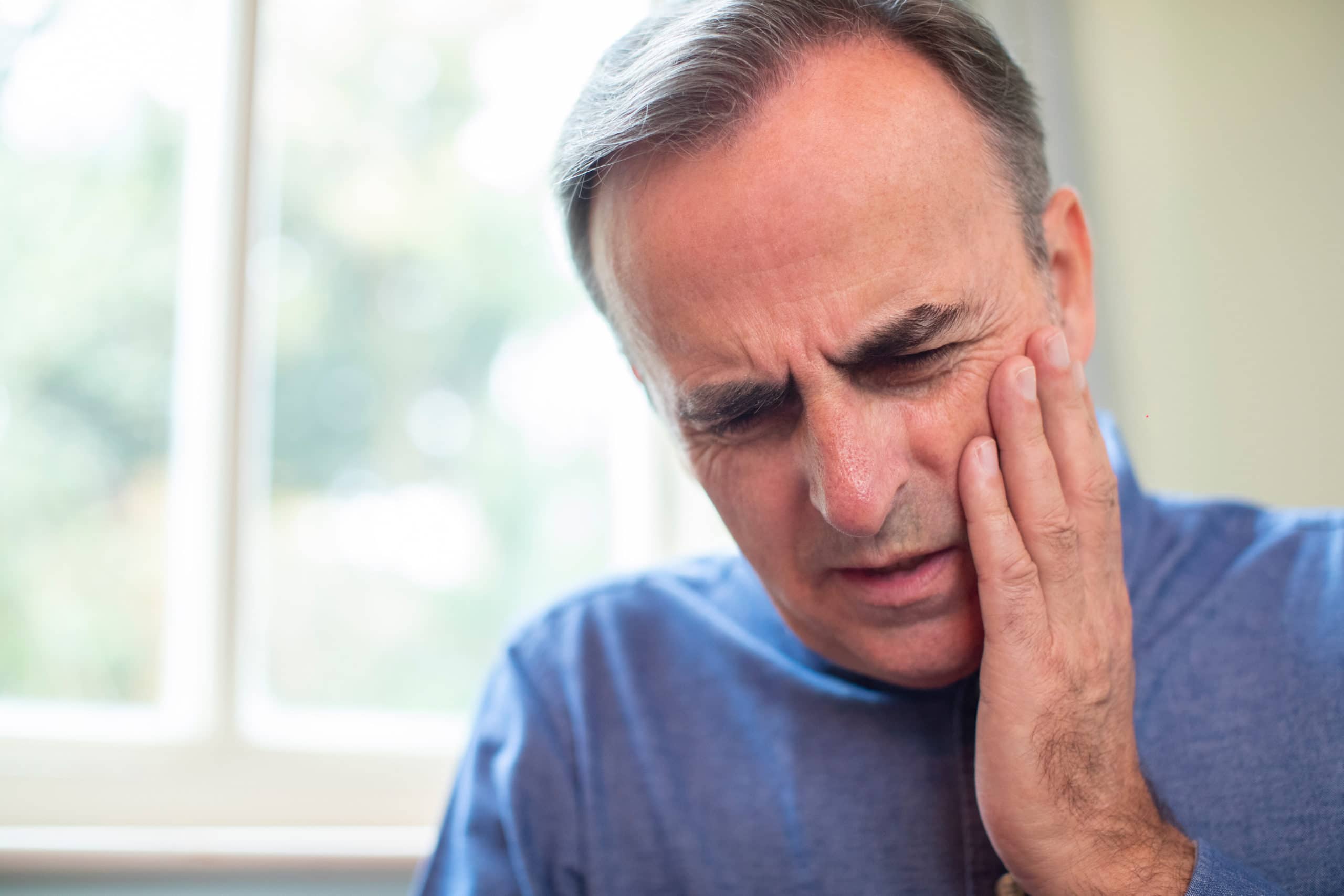 Mature Man Suffering With Toothache And Rubbing Painful Tooth